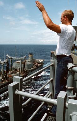 A sailor aboard the amphibious assault ship USS SAIPAN (LHA 2) signals to crewmen aboard the fleet oiler USNS NEOSHO (T-AO 143) prior to an underway replenishment off the coast of Liberia during Operation Sharp Edge. Marines embarked aboard the SAIPAN have been sent to the U.S. Embassy in Monrovia, Liberia, to augment security and evacuate U.S. and foreign nationals from the fighting between government and rebel forces