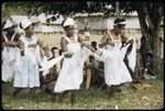 Dancers in white dresses with red trim, and musicians with bamboo instruments