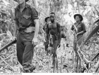 TSIMBA AREA, BOUGAINVILLE ISLAND. 1945-02-13. AN ARMED GUARD ESCORTING NATIVES CARRYING BASKETS OF PIGEONS OF THE 7TH PIGEON COMPANY ATTACHED B CORPS, CORPS OF SIGNALS THROUGH THE JUNGLE DURING A ..