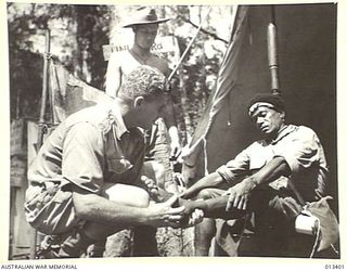 1942-10-09. CORPORAL MCNICOL, MEDICAL ORDERLY AT ONE OF OUR FORWARD POSTS IN THE NEW GUINEA JUNGLE, GIVES MEDICAL ATTENTION TO AUSTRALIAN TROOPS AND TO NATIVES PASSING THROUGH THE AREA. (NEGATIVE ..