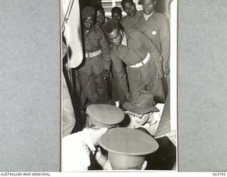 LITHGOW, NSW. 1944-01-25. AUSTRALIAN AND NEW GUINEA ADMINISTRATION UNIT NATIVES WATCHING FORGINGS BEING REMOVED FROM A SHOT BLASTING MACHINE BY MR E. C. MOORE AT THE SMALL ARMS FACTORY