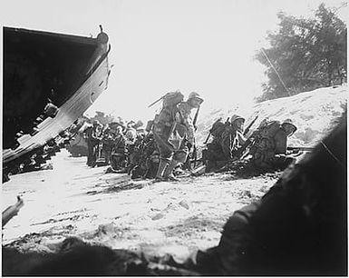 The first wave of Marines to hit the Saipan beach in the Marianas invasion take cover behind a sand dune, while waiting for the following three waves to come in.