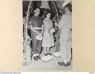 TOROKINA, BOUGAINVILLE. 1945-08-15. CORPORAL J.H. RICKARDS (1), WITH HIS BRIDE PRIVATE E.M. TOWNSEND (2), DURING THEIR MARRIAGE IN THE CHAPEL, 2/1 GENERAL HOSPITAL. THE SERVICE WAS CONDUCTED BY ..