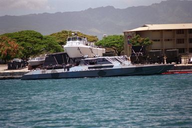 Starboard side view of two Halter Marine Mark VI combatant craft tied up in the small craft basin at Ford Island. The waterjet-powered craft have five man crews and can carry 16 SEALS and four combat rubber raiding craft for use in special operations. The boats are painted in a splinter camouflage scheme