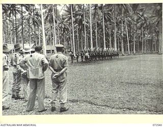 MILNE BAY, NEW GUINEA. 1944-04-20. THE HONOURABLE E.J. WARD, MINISTER FOR EXTERNAL TERRITORIES IN THE AUSTRALIAN GOVERNMENT (4), ACCOMPANIED BY AN OFFICIAL PARTY, WATCHES A ROYAL PAPUAN ..