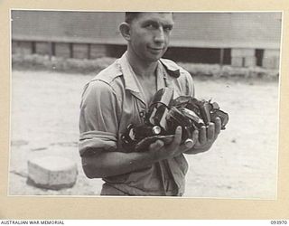 PALMALMAL PLANTATION, JACQUINOT BAY, 1945-07-10. PRIVATE H.J. BOLLMEYER, AUSTRALIAN ARMY CANTEENS SERVICE, ATTACHED 5 BASE SUB-AREA CARRYING BROKEN BOTTLES FROM THE SHED. SEVERAL TROOPS CUT THEIR ..
