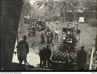 AITAPE AREA, NORTH EAST NEW GUINEA. C. 1944-04-22. HEAVY EQUIPMENT COMES ASHORE AT KORAKO VILLAGE FROM A LANDING SHIP, TANK (LST) UNDER THE WATCHFUL EYE OF RAAF GUARDS