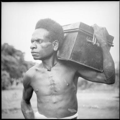 Man with a metal trunk on his shoulder, New Guinea, ca. 1936 / Sarah Chinnery