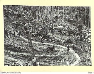 GUY'S POST - MAIN STREAM ROAD, DUMPU AREA, NEW GUINEA. 1944-04-16. NATIVE CARRIERS WORKING ON A WINDING SECTION OF THE ROAD. GRADING EXPEDIENTS ARE NECESSARY TO OVERCOME THE STEEP 300 FOOT DESCENT ..