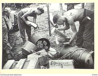 BARARA, BOUGAINVILLE ISLAND. 1945-03-07. QX34456 PRIVATE M.J. CUSKELLY (1) AND QX60776 PTE E.J. MCKEE (2) 25TH INFANTRY BATTALION UNPACKING FRESH BREAD FROM A STORPEDO, ONE OF MANY, WHICH ARE ..