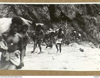 FARIA RIVER, NEW GUINEA. 1944-01-11. NATIVE CARRIERS, LOADED WITH RATIONS AND AMMUNITION FOR NO. 11 PLATOON, B COMPANY, 2/9TH INFANTRY BATTALION CROSSING THE FARIA RIVER JUST ABOVE GUY'S POST