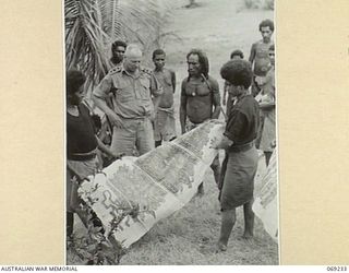 MENDAROPU, NEW GUINEA. 1942-10. P391 CAPTAIN B.W. FAITHORN, AUSTRALIAN AND NEW GUINEA ADMINISTRATIVE UNIT, INSPECTING TAPA CLOTH, HELD BY MEMBERS OF THE ROYAL PAPUAN CONSTABULARY. THIS CLOTH WAS ..