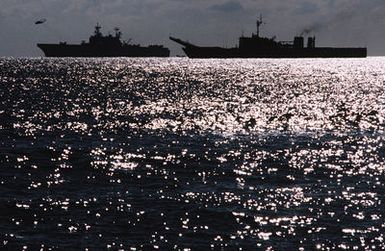 A silhouetted port beam view of the amphibious assault ship USS SAIPAN (LHA-2) and the tank landing ship USS BARNSTABLE COUNTY (LST-1197) underway during Exercise Crisex '81