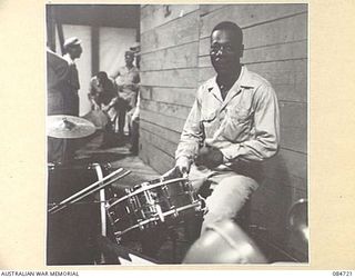LAE, NEW GUINEA. 1944-11-23. A NEGRO DRUMMER WHO WAS A MEMBER OF THE FAMOUS CAB CALLOWAY ORCHESTRA IN AMERICA, REHEARSING WITH AN AMERICAN SPECIAL SERVICE BRANCH BAND TO ENTERTAIN AUSTRALIAN TROOPS ..