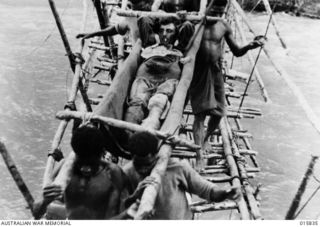 1943-09-28. NEW GUINEA. ADVANCE ON SALAMAUA. NATIVE BEARERS CARRY A WOUNDED AUSTRALIAN OVER A ROUGH BRIDGE ACROSS THE FRANCISCO RIVER. THE AUSTRALIAN WAS WOUNDED IN THE KNEE AND LEG AND WAS FOUR ..