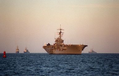 A starboard bow view of the amphibious assault ship USS GUAM (LPH-9) entering the roadstead upon returning from sea following the passage of Hurricane Felix out of the area. The Spruance-class destroyers USS DEYO (DD-989), USS ARTHUR W. RADFORD (DD-968) and USS JOHN ROGERS (DD-983) are following behind the GUAM