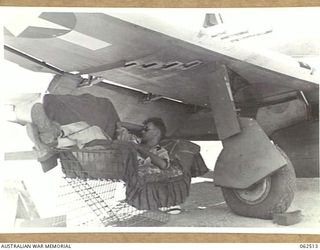 NEW GUINEA. 1944-01-05. A UNITED STATES ARMY AIR FORCE MECHANIC ENJOYS A QUIET SLEEP UNDER THE MAINPLANE OF HIS AIRCRAFT