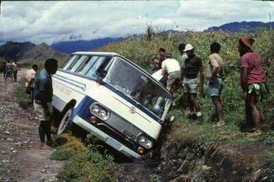 “Bus in the ditch, Mt. Hagen”(original caption). Bus has driven into the ditch, men are spinning around.