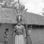 Portrait of man in costume with elaborate headdress, outside a house