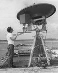 Principal electronics technician David Havens turns the wheel which adjusts vertical angle on the new satellite weather antenna, state of the art antenna for its time, installed aboard D/V Glomar Challenger (ship) during the port call at Agana, Guam, between Legs 59 and 60 of the Deep Sea Drilling Project. The big wheel at the bottom takes care of the horizontal angle. Shipboard data tables are provided for the required horizontal and vertical antenna angles. Information is received from a satellite in stationary orbit and processed by shipboard equipment to produce a weather map which enables the captain, scientists and operations personnel to get weather forecasts 18 hours in advance at any drilling and coring site. 1978