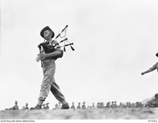 LAE, NEW GUINEA. 1944-06-08. PERSONNEL OF THE 2/7TH ADVANCED WORKSHOP MARCHING ON THE UNIT PARADE GROUND LED BY THEIR PIPER VX117889 CRAFTSMAN CURRAN