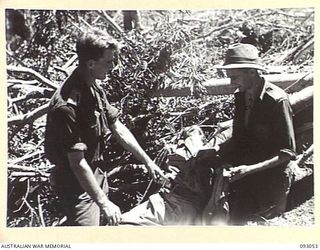 WEWAK AREA, NEW GUINEA, 1945-06-11. LT T.R. ERSKINS (1) AND CPL L. ALLEN (2), MEMBERS OF 2/8 INFANTRY BATTALION, SEARCH A DEAD JAPANESE FOR PAPERS. HE IS THOUGHT TO HAVE BEEN THE CAPTAIN IN CHARGE ..