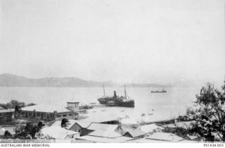 VIEW OF THE HARBOUR FROM A STREET IN THE TOWN, SHOWING THE OIL TANKER PHYSA IN THE BACKGROUND AND HMAT KANOWNA AT THE END OF THE WHARF. (ORIGINAL PRINT HELD IN AWM PR91/102)