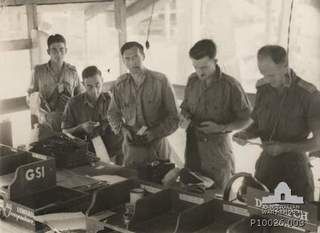 Informal group portrait of Australian Soldiers of General Staff Intelligence (GSI) sorting correspondance and despatches on the day of the Japanese surrender. Identified, fourth from left, is ..