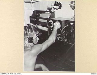 S9835 HORACE LYLE INGRAM IN THE WIRELESS ROOM OF THE MOTOR LAUNCH 825, ROYAL AUSTRALIAN NAVY. THE VESSEL IS THE ONLY MOTOR LAUNCH IN THE SOUTH WEST PACIFIC AREA TO BRING DOWN A JAPANESE AIRCRAFT