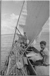 Canoes: men on outrigger canoe with sails up, paddles on platform, man (r) sits on fishing net