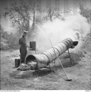 CAPE WOM, WEWAK AREA, NEW GUINEA. 1945-08-29. PRIVATE F.A. HUBBARD, 110 BRIGADE WORKSHOP, CORPS OF AUSTRALIAN ELECTRICAL AND MECHANICAL ENGINEERS, FIRING AN INCINERATOR MADE FROM 44 GALLON DRUMS