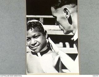 NEW GUINEA. 1942-08. THIS YOUNG PAPUAN BOY HAD SUFFERED A SERIOUS BOIL INFECTION OF THE FACE. HERE, CAPTAIN P. JENSON, THE COMMANDER OF NATIVE MEDICAL SERVICES IS SEEN INSPECTING THE AFFECTED JAW