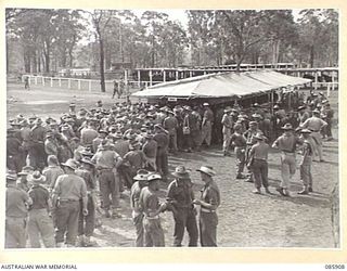 HERBERTON, QLD. 1945-01-20. HQ 9 DIVISION PUNTERS COLLECTING WINNINGS FROM THE PAY OUT WINDOWS OF THE TOTE DURING THE 9 DIVISION GYMKHANA AND RACE MEETING AT HERBERTON RACECOURSE. THREE TOTES WERE ..