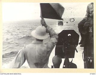 AT SEA, NEW GUINEA. 1944-06-01. 01102183 LIEUTENANT J CAVANAUGH, THE MEMBER OF AN ENGINEER BOAT AND SHORE REGIMENT, UNITED STATES ARMY, (1), SIGNALLING AMERICAN LANDING BARGES WHICH ARE CARRYING ..