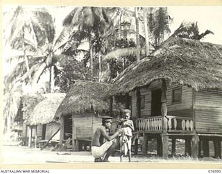 JACQUINOT BAY, NEW BRITAIN. 1944-11-17. A TULTUL (GOVERNMENT CHIEF) AND HIS BABY SON IN MALMAL VILLAGE