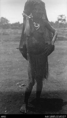 Woman in grass skirt carrying bag on head near Atemble