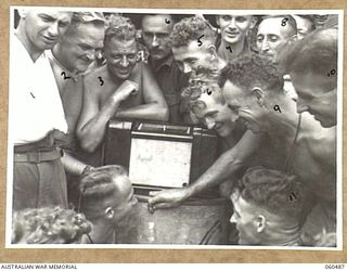 DUMPU, NEW GUINEA. 1943-11-13. TROOPS OF HEADQUARTERS, 7TH AUSTRALIAN DIVISION GATHERED AROUND THE RADIO SET LISTENING TO THE RESULTS OF THE MELBOURNE CUP. SHOWN ARE: CORPORAL R. HASTINGS (1); ..