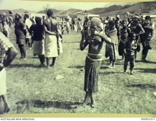 PAPUA NEW GUINEA, 1965. A NATIVE GIRL PLAYING HER FLUTE TO THE PILOT OF ONE OF THE DC4 TRANSPORTS, WHILE OTHER NATIVES CROWD AROUND THE AIRFIELD