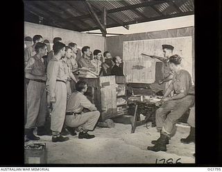MOMOTE, LOS NEGROS ISLAND, ADMIRALTY ISLANDS. C. 1944-04. INFORMAL GROUP PORTRAIT OF OFFICERS AND NON COMMISSIONED OFFICER PILOTS OF NO. 76 (KITTYHAWK) SQUADRON RAAF BEING BRIEFED BY THE COMMANDING ..