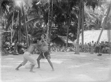 [Two young men wrestle while crowd watches]