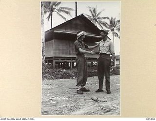 PALMALMAL PLANTATION, JACQUINOT BAY, NEW BRITAIN, 1945-08-15. CORPORAL P. BECKER, PUBLIC RELATIONS HEADQUARTERS 11 DIVISION CEMENTS THE ALLIED VICTORY WITH A HANDSHAKE FROM AN AMERICAN SERVICEMAN ..
