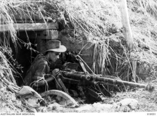 Wewak, New Guinea. May 1945. An Australian 6th Division AIF soldier examines a captured Japanese 20mm gun in front of a camouflaged Japanese position on the Wewak Peninsula