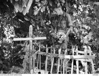 PUL PUL, NEW BRITAIN. 1945-01-17. NX51929 SERGEANT A.N. TAYLOR, "B" COMPANY, 1ST NEW GUINEA INFANTRY BATTALION, PLACING FLOWERS ON THE GRAVE OF PRIVATE D. MCLENNAN OF THE 2/22ND INFANTRY BATTALION ..