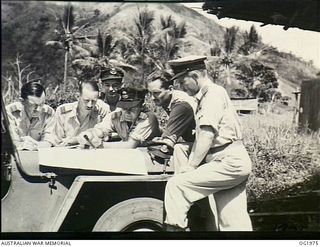 VIVIGANI, GOODENOUGH ISLAND, PAPUA. C. 1944-10. WING COMMANDER (WG CDR) HUGH CONAGHAN, COOLANGATTA, QLD, DRAWS A MAP-POINT TO THE ATTENTION OF WG CDR BRIAN WADDY, FREWVILLE, SA, SECOND FROM RIGHT, ..