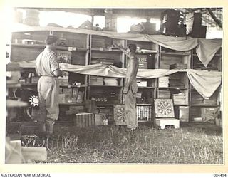 LAE AREA, NEW GUINEA. 1944-12-20. SENIOR REPRESENTATIVE GREEN, YMCA, (1), WITH CORPORAL V T STANFORD, (2), LOOKING OVER STOCK. THE EQUIPMENT INCLUDES GAMES, WIRELESS SETS AND A PUBLIC ADDRESS ..