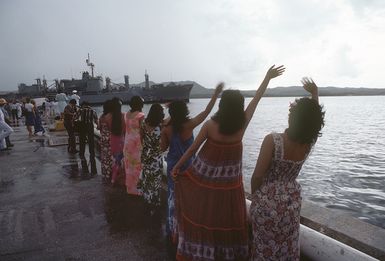 A crowd waves and welcomes the crew of the combat stores ship USS NIAGARA FALLS (AFS 3) upon the ship's arrival at Naval Station Guam