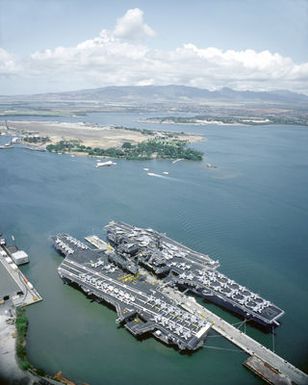 The aircraft carriers USS MIDWAY (CV-41), lower left, and USS INDEPENDENCE (CV-62) lie tied up at the naval station. The midway is en route from Naval Station, Yokosuka, Japan, to Naval Air Station, North Island, Calif., where it will be decommissioned in the spring of 1992. The Independence will travel to Yokosuka to take over as the Navy's forward-based aircraft carrier. The USS Arizona Memorial and Ford Island are in the background