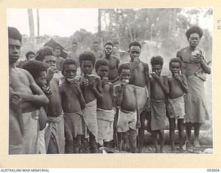 MOROKAIMORO, BOUGAINVILLE, 1945-06-05. PICCANINNIES EATING WHEATMEAL CAKES. THE RATIONS HAVE BEEN SUPPLIED BY ANGAU. THE NATIVES, EVACUATED FROM ENEMY AREAS, ASSIST GREATLY BY SCOUTING AND LOCATING ..