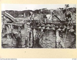 MADANG, NEW GUINEA. 1944-05-21. AUSTRALIAN TROOPS GRAPPLING FOR ABANDONED JAPANESE EQUIPMENT ALONGSIDE THE WHARF