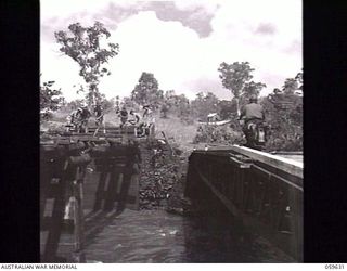 DONADABU, NEW GUINEA. 1943-11-03. TROOPS OF NO. 3 PLATOON, 18TH AUSTRALIAN FIELD PARK COMPANY, ROYAL AUSTRALIAN ENGINEERS, REBUILDING A BRIDGE (LEFT) OVER THE EWARIGO CREEK. A TEMPORARY SMALL BOX ..